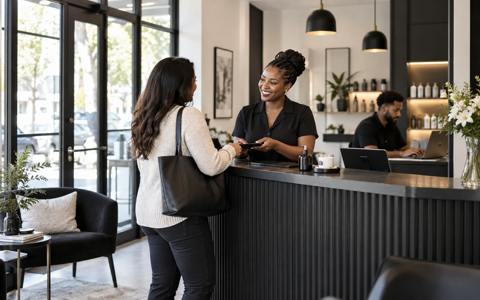 A business owner serving a customer while a colleague handles an online enquiry
